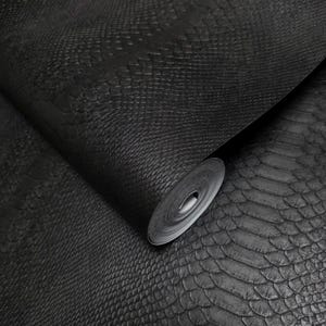 May include: A roll of wallpaper featuring a textured black surface with a repeating snakeskin pattern. The material has a matte finish and a detailed, embossed scale design that mimics the appearance of reptile skin across the entire surface.