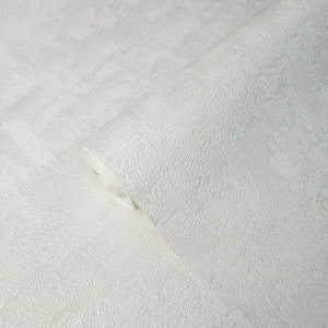 May include: A roll of textured, off-white wallpaper. The paper has a subtle, mottled appearance and a slightly raised, tactile surface. The roll is partially unrolled, revealing the interior of the roll. The overall effect is a neutral, versatile design suitable for various interior styles.