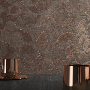 May include: Two copper mugs on a dark wood surface in front of a textured copper wall. The wall has a pattern of overlapping geometric shapes.
