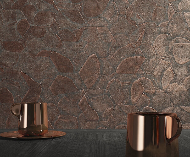 May include: Two copper mugs on a dark wood surface in front of a textured copper wall. The wall has a pattern of overlapping geometric shapes.