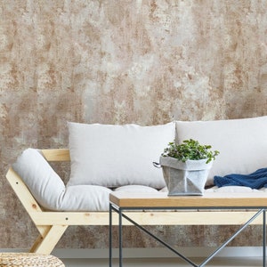 May include: A white couch with two pillows sits in front of a wall with a brown and white textured wallpaper. A small potted plant sits on a wooden coffee table with black metal legs.