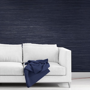May include: A white couch with a blue throw blanket in front of a dark blue textured wall.