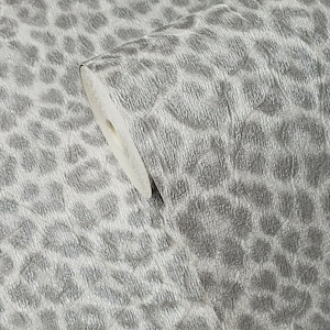 May include: A roll of silver wallpaper with a textured leopard print design. The wallpaper has a metallic sheen and a repeating pattern of irregular, rounded shapes. The roll is partially unrolled, revealing the white backing.
