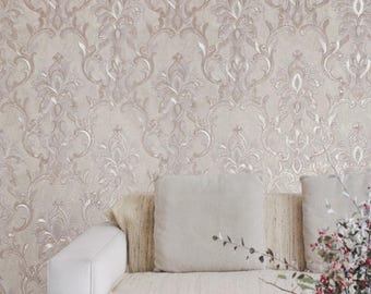 May include: A beige and silver damask wallpaper covers a wall. A white sofa with two square pillows and a beige throw is in front of the wall. A sprig of red berries and green leaves is on the right.