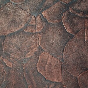 May include: Close-up of a textured fabric with a geometric pattern. The fabric is a dark brown colour with a subtle sheen.