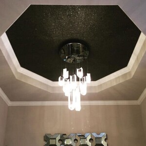 May include: A black ceiling with glitter, a white trim, and a crystal chandelier hanging from the center.