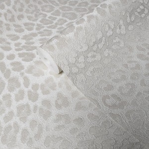 May include: A roll of light gray wallpaper with a textured leopard print pattern. The wallpaper is partially unrolled, revealing the pattern and texture. The design features large, irregular spots.