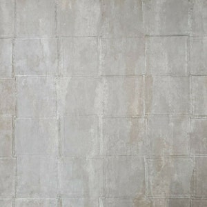 May include: A close-up of a gray concrete wall with a grid pattern. The wall is made of square tiles with visible grout lines.