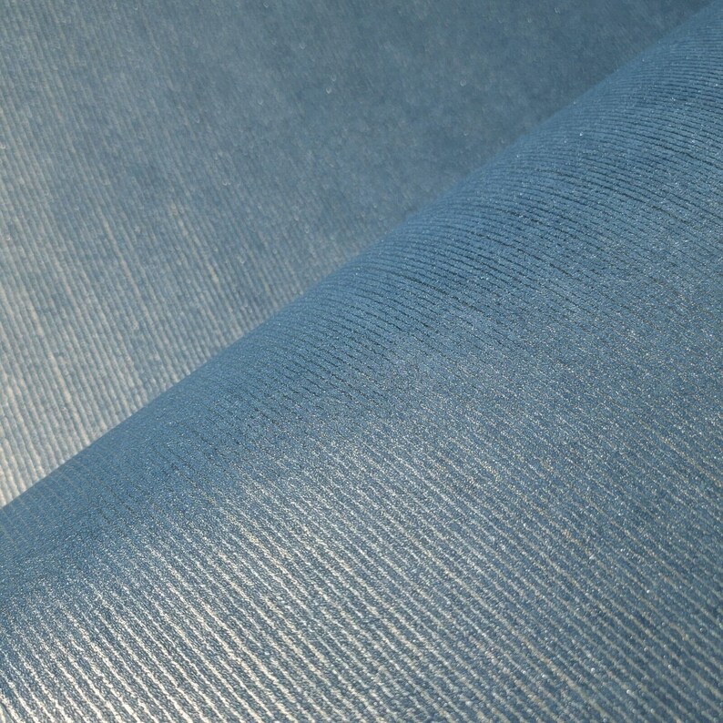 Puede incluir: Primer plano de una tela azul con una superficie texturizada y acanalada. La tela est&aacute; doblada por la mitad, creando una l&iacute;nea diagonal.
