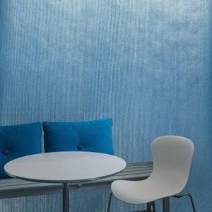 Puede incluir: Una mesa redonda blanca con un banco acolchado azul y una silla blanca. La mesa y el banco est&aacute;n frente a una pared azul texturizada.