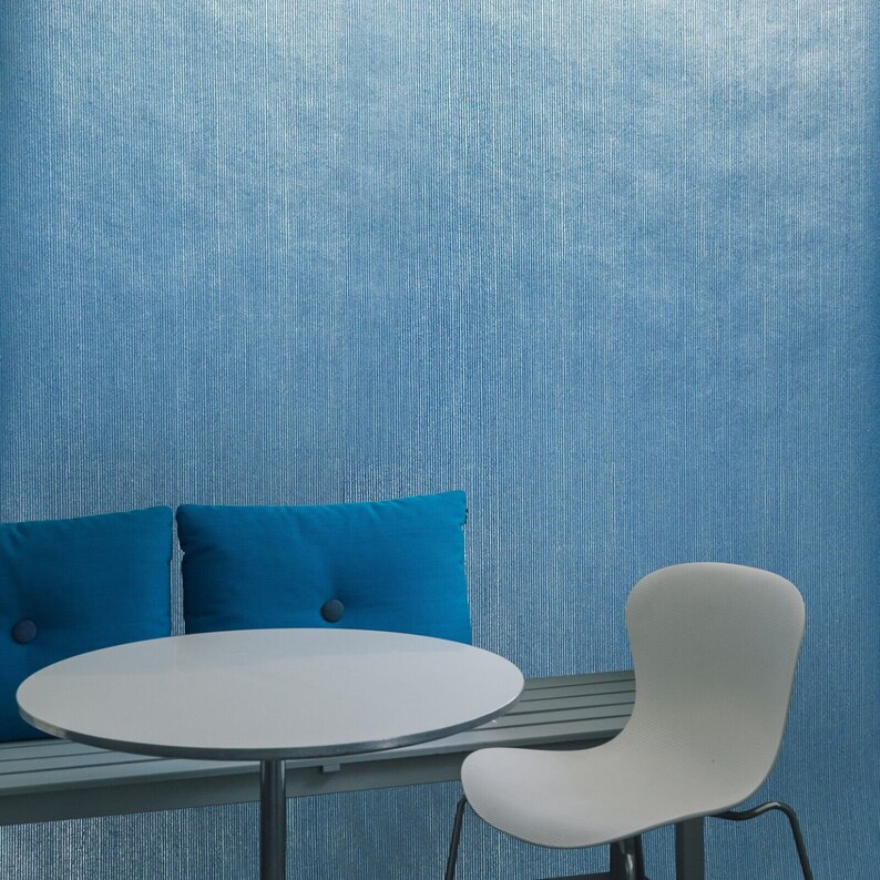 Puede incluir: Una mesa redonda blanca con un banco acolchado azul y una silla blanca. La mesa y el banco est&aacute;n frente a una pared azul texturizada.