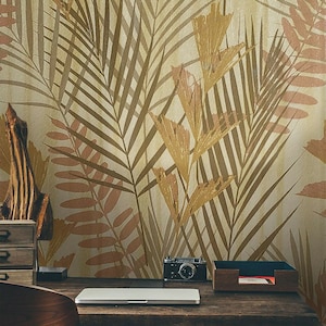May include: A home office desk with a laptop, camera, and a wooden organizer. The wall behind the desk is covered in a wallpaper with a brown and beige tropical leaf pattern.
