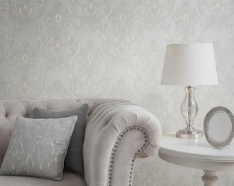 May include: A light gray tufted sofa with decorative pillows, a white table lamp, and a small framed mirror. The background features a light gray damask wallpaper with a repeating floral pattern. The scene evokes a sense of classic elegance.