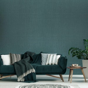May include: A dark green sofa with a throw blanket and pillows in a living room with a teal green wall.