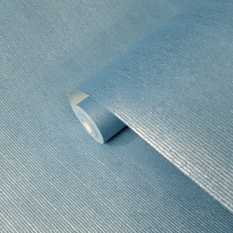 Puede incluir: Un rollo de papel tapiz azul texturizado con un brillo sutil. El papel tapiz tiene un patr&oacute;n acanalado y est&aacute; enrollado.