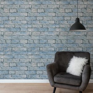 May include: A room featuring a blue brick wall, a dark gray armchair with a white fluffy pillow, a black pendant light, and light brown wood flooring. The brick wall has a distressed, textured appearance.