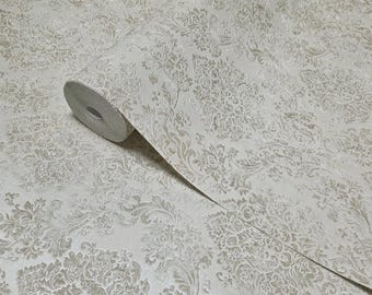 May include: A roll of off-white wallpaper with a raised, ornate floral pattern in a muted gold color. The wallpaper is partially unrolled, revealing the intricate design and texture. The overall aesthetic is classic and elegant.