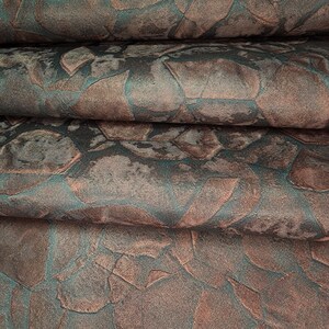 May include: Close-up of a fabric with a textured, geometric pattern in shades of teal and brown. The fabric is folded in layers, creating a sense of depth and dimension.