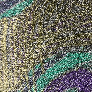 May include: Close-up of a textured surface with a gold, green, and purple color scheme. The surface has a metallic sheen and appears to be made of a fine-grained material.