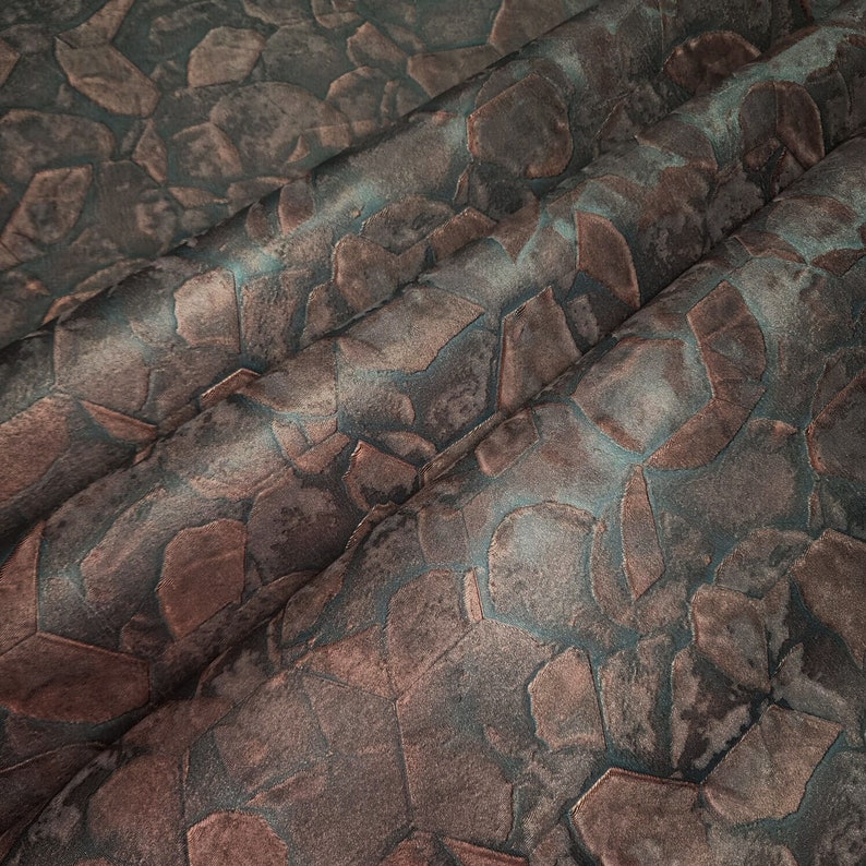 May include: Close-up of a fabric with a textured geometric pattern in shades of brown and blue. The fabric has a subtle sheen and a soft, luxurious feel.