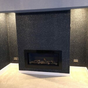 May include: A black fireplace with a black glass firebox and a log set. The fireplace is surrounded by a black glitter wall.