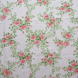 May include: White fabric with a repeating pattern of pink roses and green leaves. The roses are clustered in groups, and the leaves form a delicate, winding design across the fabric. The overall effect is a classic, floral print.