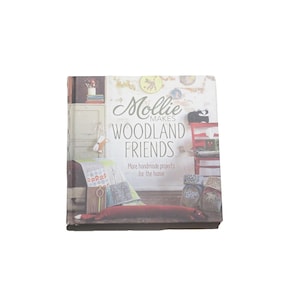 May include: A square book titled "Mollie Makes Woodland Friends" featuring handmade projects for the home. The cover displays a cozy interior scene with a red chair, a black cat, and various craft items.