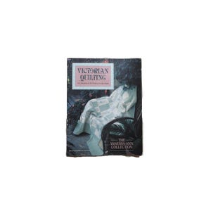 May include: A book cover titled "Victorian Quilting" with a picture of a quilt draped over a chair. The cover has a dark background with the text in a white and pink box. The book is part of "The Vanessa-Ann Collection."