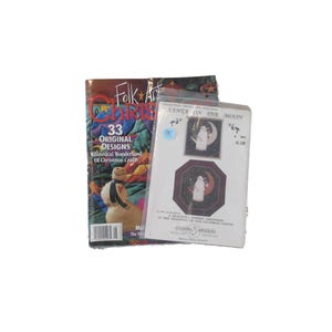 May include: Two magazines are displayed. One is titled "Folk Art Christmas" with "33 Original Designs" and a snowman graphic. The other is a pattern packet labeled "Santa on the Moon" with two images of Santa and the moon.
