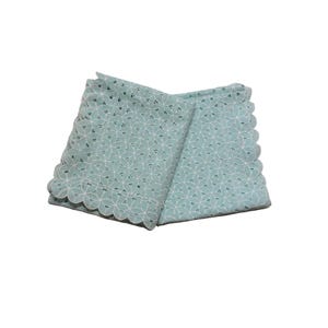 May include: Folded, light teal cloth napkin with a scalloped edge. The napkin features a repeating floral pattern in white. The fabric appears to be a delicate, open-weave design, suitable for decorative use.