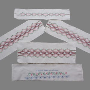 Può includere: Diversi pezzi di tessuto bianco con ricami. I pezzi presentano motivi ripetuti in rosa, verde e marrone. Un pezzo ha il testo "A friend loveth at all times" con ricami floreali.