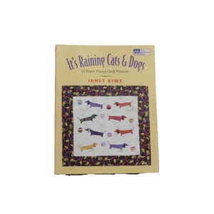 May include: A book titled "It's Raining Cats & Dogs" with a colorful quilt design on the cover. The quilt features dachshunds in various colors and patterns. The book is by Janet Kime and is for 32 paper-pieced quilt projects.