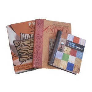 May include: A stack of four books with various covers. One book has a pillow with a zebra print on the cover. Another book is titled "The Practical Guide to Decorative Antiques". The last book is titled "The Paint Effects Bible".