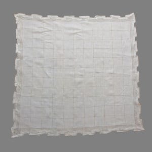 May include: A white, square-shaped textile with a grid pattern and a decorative, scalloped edge. The fabric appears to be lightweight and possibly linen or cotton. The overall design is simple and elegant.