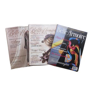 May include: Three fashion magazines titled "Belle Armoire" are displayed. The covers feature various designs, including jewelry, clothing, and accessories. The magazines have a glossy finish and are stacked on a white surface.
