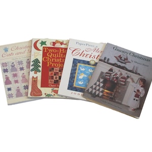 May include: A stack of four Christmas-themed books. The titles include "Christmas Cats and Quilts to Celebrate", "Two-Hour Quilted Christmas Projects", "Paper Piece a Merry Christmas", and "Country Christmas". The covers feature festive illustrations.
