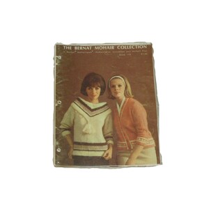 May include: Vintage knitting pattern book titled "The Bernat Mohair Collection." The cover features two women modeling mohair sweaters. The book has a brown cover with the title in white text. The women are wearing sweaters in shades of cream, brown, and orange.