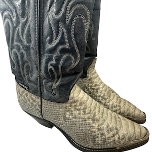 May include: Pair of cowboy boots with a snakeskin pattern on the foot and a dark blue leather upper with decorative stitching. The boots have pointed toes and a stacked heel.