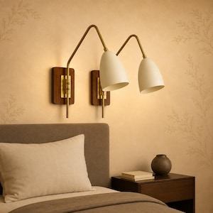 Può includere: Due lampade da parete con paralumi conici color bianco sporco opaco, bracci in metallo color ottone e piastre rettangolari in legno scuro. Gli apparecchi sono posizionati fianco a fianco, ciascuno con un braccio regolabile.