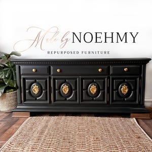 May include: Black painted wooden sideboard with four doors and gold hardware. The sideboard has a carved design on the doors and sits on a wooden base. The text "Made by NOEHMY REPURPOSED FURNITURE" is above the sideboard.