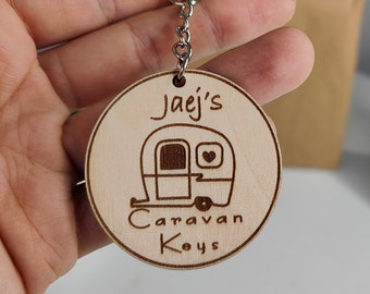 Puede incluir: Un llavero de madera con el texto "Jaej's Caravan Keys" y una pequeña ilustración de una caravana con un corazón en la ventana.