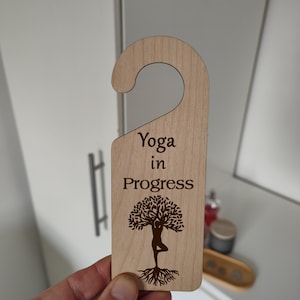 May include: Wooden door hanger with a brown tree and a person in a yoga pose. The text "Yoga in Progress" is printed on the hanger.