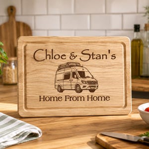 May include: A wooden chopping board with the engraved text "Chloe & Stan's" above an illustration of a camper van. The words "Home From Home" are engraved below the van. The board is rectangular with a juice groove.