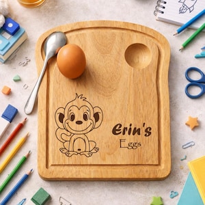 以下が含まれることがあります： 木製のまな板。猿のイラストと「Erin's Eggs」の文字。卵とスプーンがまな板の上にあります。オレンジジュース、色鉛筆、ロケットの絵が描かれたメモ帳などのアイテムも含まれています。
