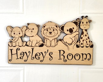 May include: Wooden door sign with a light brown finish featuring a line of cartoon animals including an elephant, hippopotamus, lion, koala, and giraffe. The sign reads "Hayley's Room" in a decorative font.