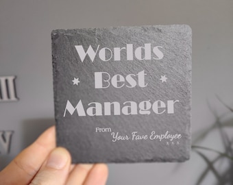 May include: A black slate coaster with the text "Worlds Best Manager" in white lettering. The text "From Your Fave Employee xxx" is also in white lettering.