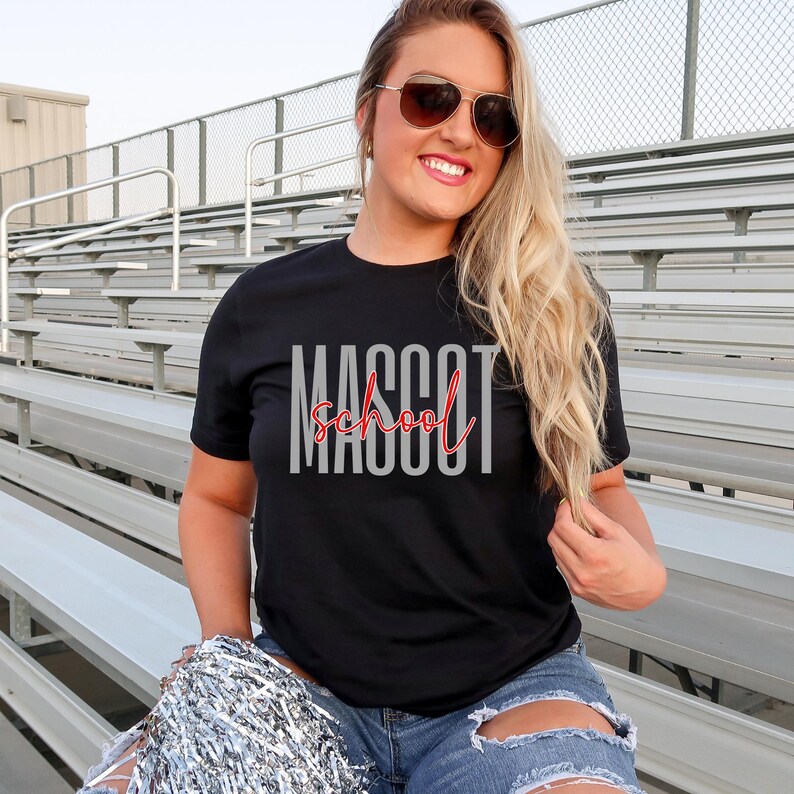 Może przedstawiać: Czarny t-shirt z kr&oacute;tkim rękawem z napisem MASCOT wykonanym dużymi szarymi wielkimi literami oraz słowem school napisanym czerwoną kursywą na środku. Koszulka posiada okrągły dekolt oraz standardowy kr&oacute;j.
