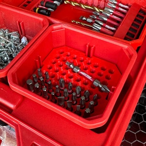 May include: A red plastic tool organizer with a honeycomb-shaped insert. The insert holds a variety of small tools, including a red and black screwdriver bit. The organizer is labeled "Milwaukee".