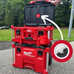 May include: A red and black Milwaukee Packout tool box with a black lid that is open. The lid has a red button on the top. The tool box is on wheels and has a handle.