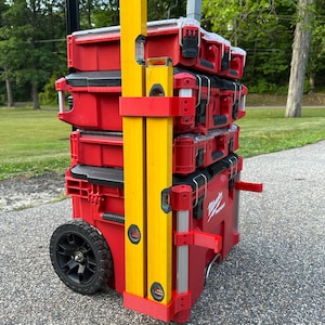 May include: A stack of red toolboxes with a yellow and silver level attached. The toolboxes are on wheels and have a black handle.
